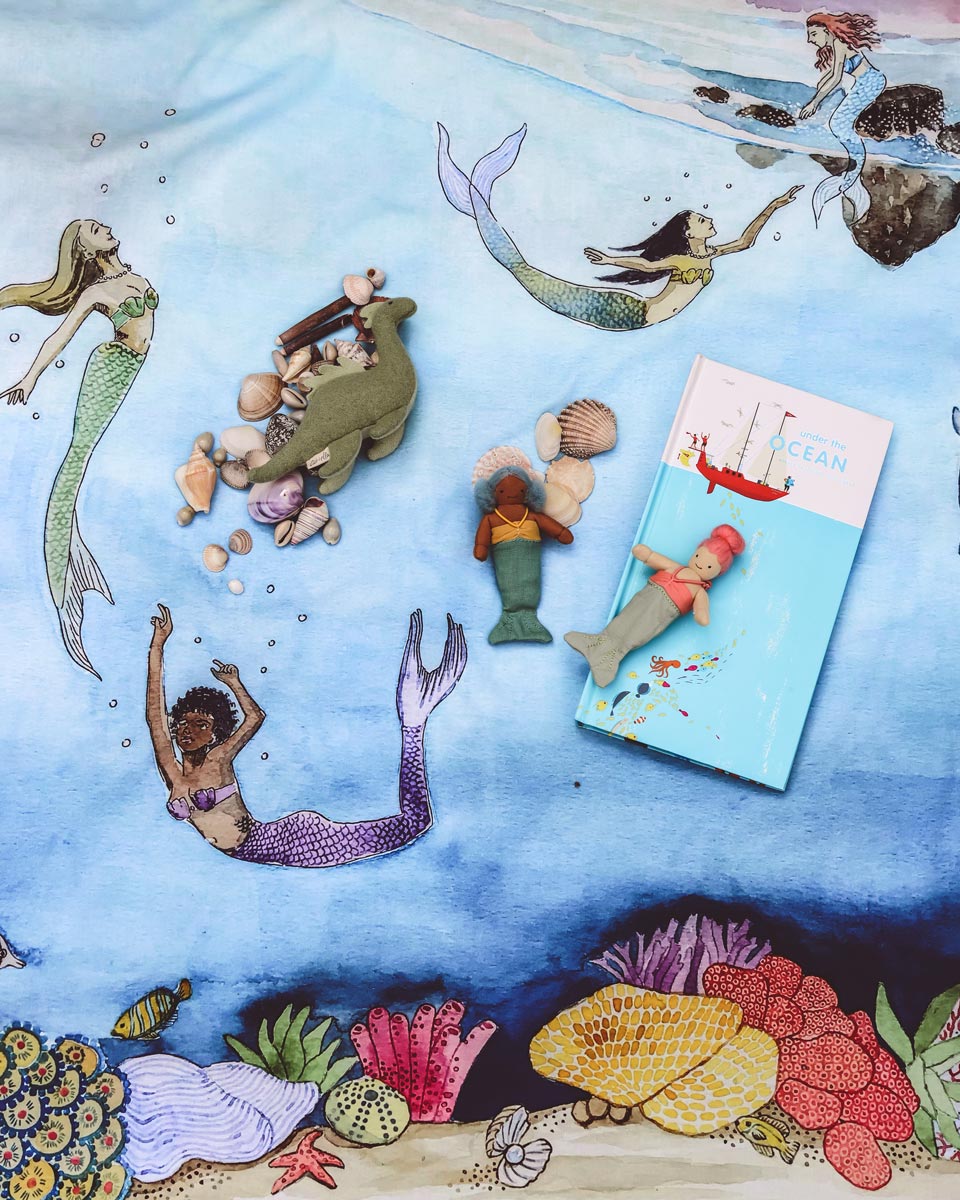 Wondercloths childrens mermaid ocean print play silk laid on the floor with some soft toy mermaids and sea creatures on top