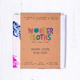 WonderCloths soft in bloom play silk folded up in its card sleeve packaging on a white wooden background