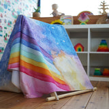 A giant Wonderie play cloth with the magical sky design placed over a Triclimb climbing frame to create a den. Shelves filled with toys can be seen in the background. 