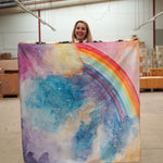 A person holding up a giant Wonderie play cloth featuring the magical sky design which features a rainbow. 