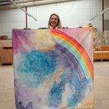 A person holding up a giant Wonderie play cloth featuring the magical sky design which features a rainbow. 