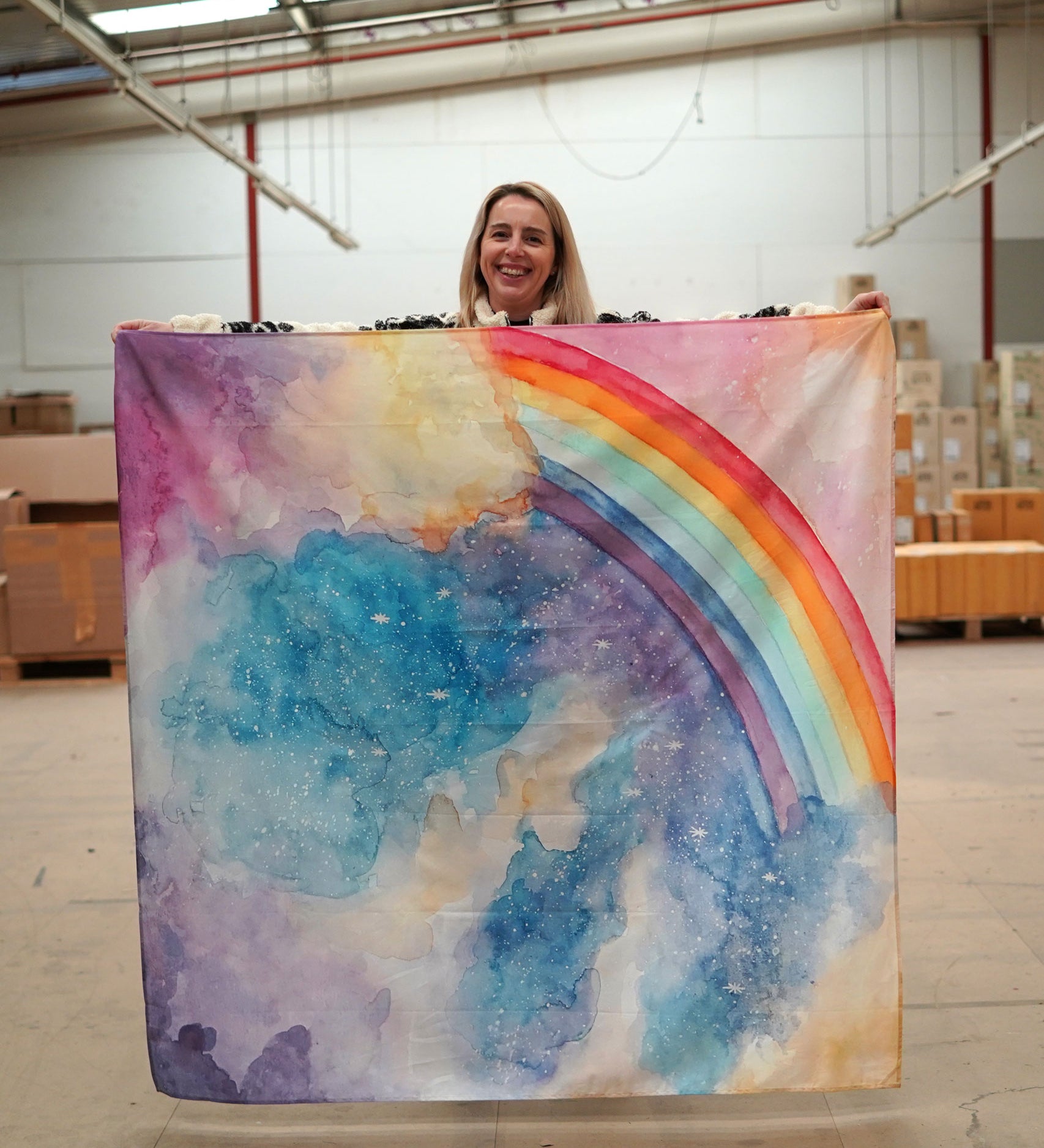 A person holding up a giant Wonderie play cloth featuring the magical sky design which features a rainbow. 