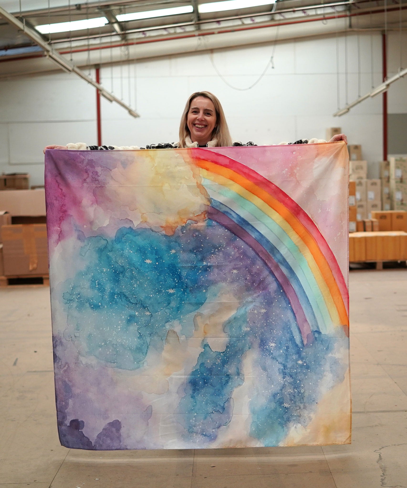 A person holding up a giant Wonderie play cloth featuring the magical sky design which features a rainbow. 