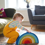 A child crouching down besides the Grimm's Gwawr Sunrise 12 Piece Rainbow. 