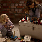 2 children playing with the Wooden Story 30 Rainbow Blocks in Tray. One child is sat on the floor the other is sat on top of a painted wooden chest. 