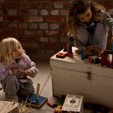 2 children playing with the Wooden Story 30 Rainbow Blocks in Tray. One child is sat on the floor the other is sat on top of a painted wooden chest. 