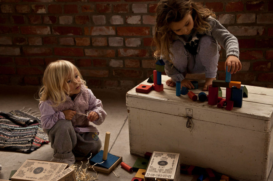 2 children playing with the Wooden Story 30 Rainbow Blocks in Tray. One child is sat on the floor the other is sat on top of a painted wooden chest. 