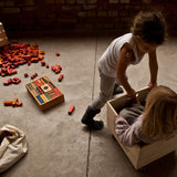 Wooden Story Rainbow Blocks in Tray on the floor with children playing next to them. A wooden box can be seen in the background surrounded by yellow and orange blocks. 