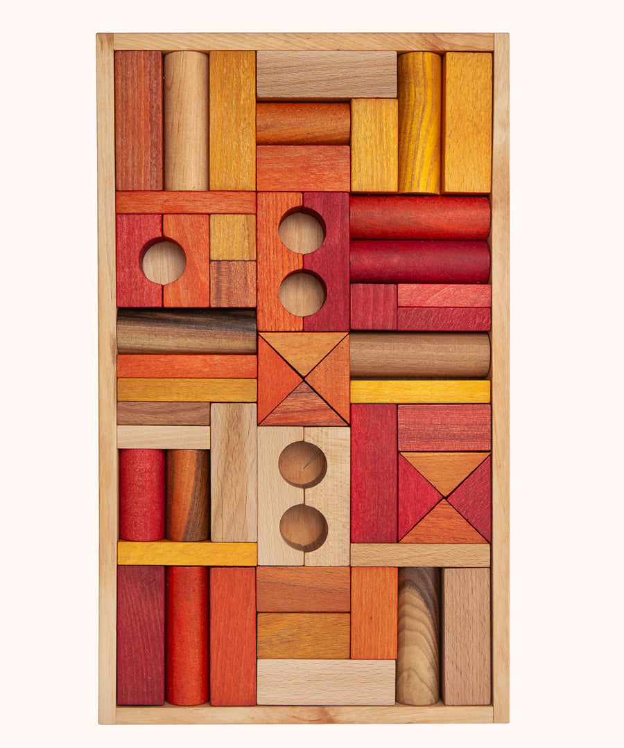 Wooden Story 54 Warm Blocks in Tray on a plain background. The set features various shapes of wooden clocks in warm orange, natural and yellow shades. 