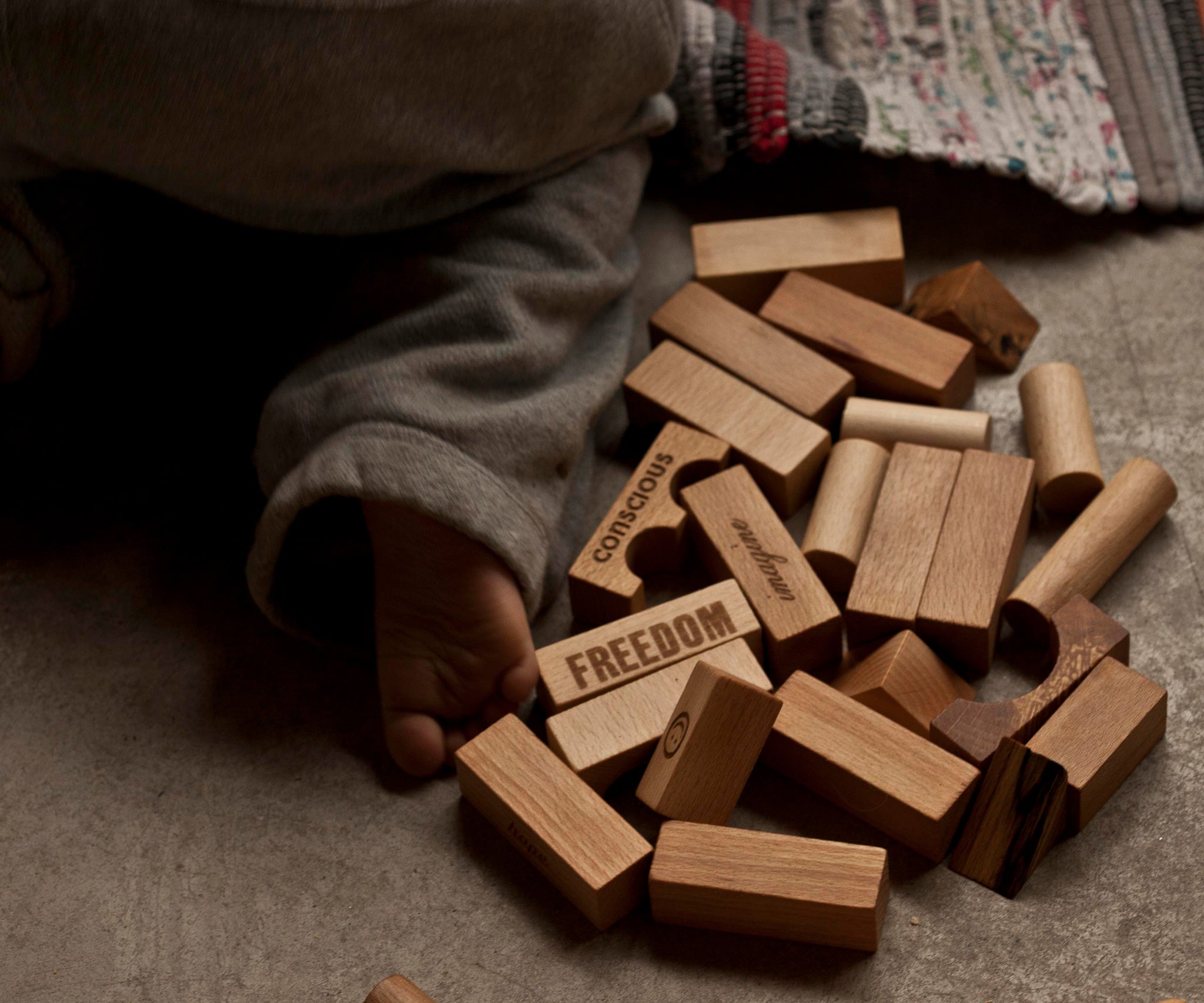 A collection of natural Wooden Story blocks on the floor, a child's foot can be seen besides them.