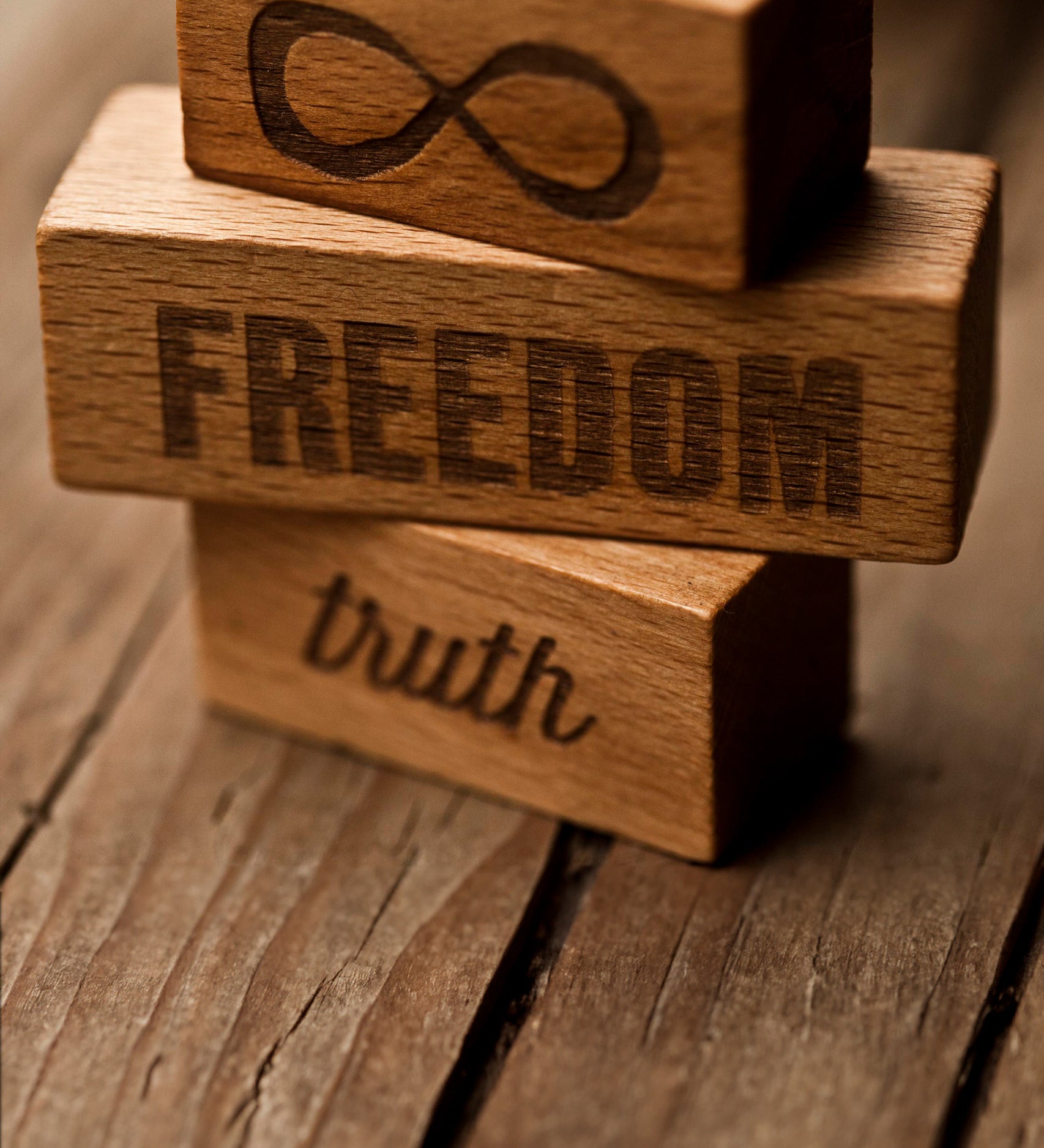 A close up of three blocks from the Wooden Story 72 XL Peace & Love Blocks set. One block has the infinity symbol, one has the word freedom and the third has the word truth etched on. 