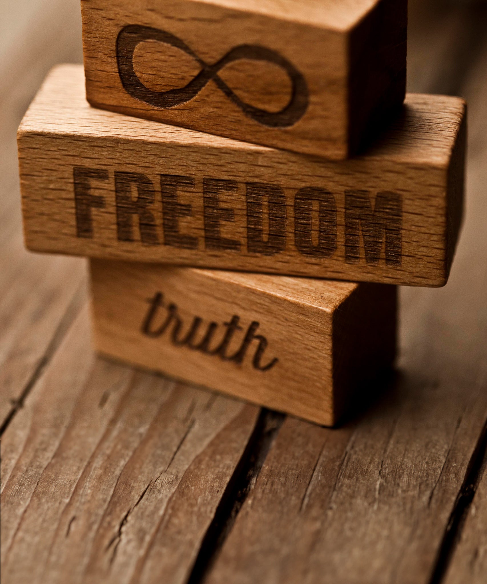 A close up of three blocks from the Wooden Story 72 XL Peace & Love Blocks set. One block has the infinity symbol, one has the word freedom and the third has the word truth etched on. 