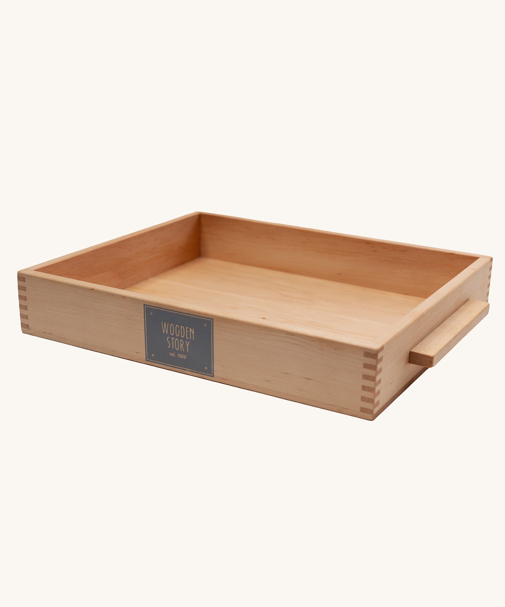 The tray from the Wooden Story Montessori Sand Tray set shown on a plain background pictured at .n angle showing the dovetail style joints of the tray and the logo printed on the front. 