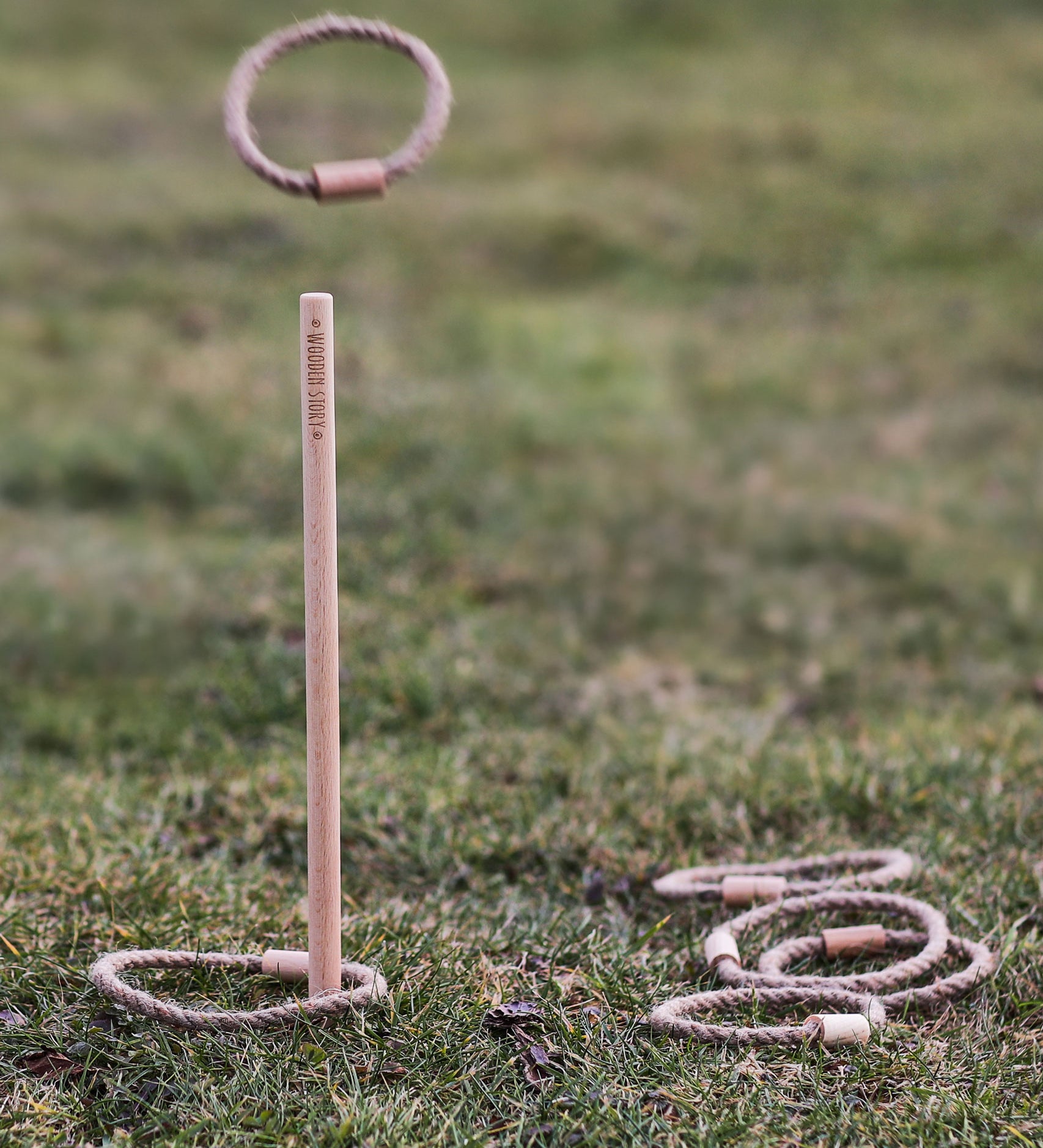 The Wooden Story Loop Toss game set up on grass outdoors. A rope loop  can be seen mid air.