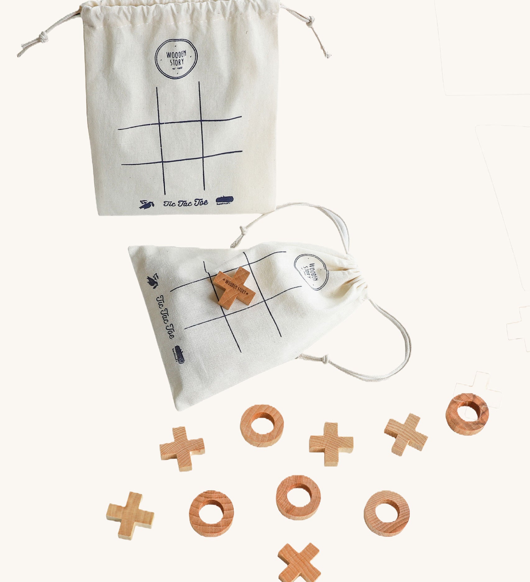 Wooden Story Tic Tac Toe game on a plain background. The wooden X and O pieces are spread out besides the drawstring bag which has the grid printed on it. One wooden X cross piece has been placed on the grid in the centre of the bag. 