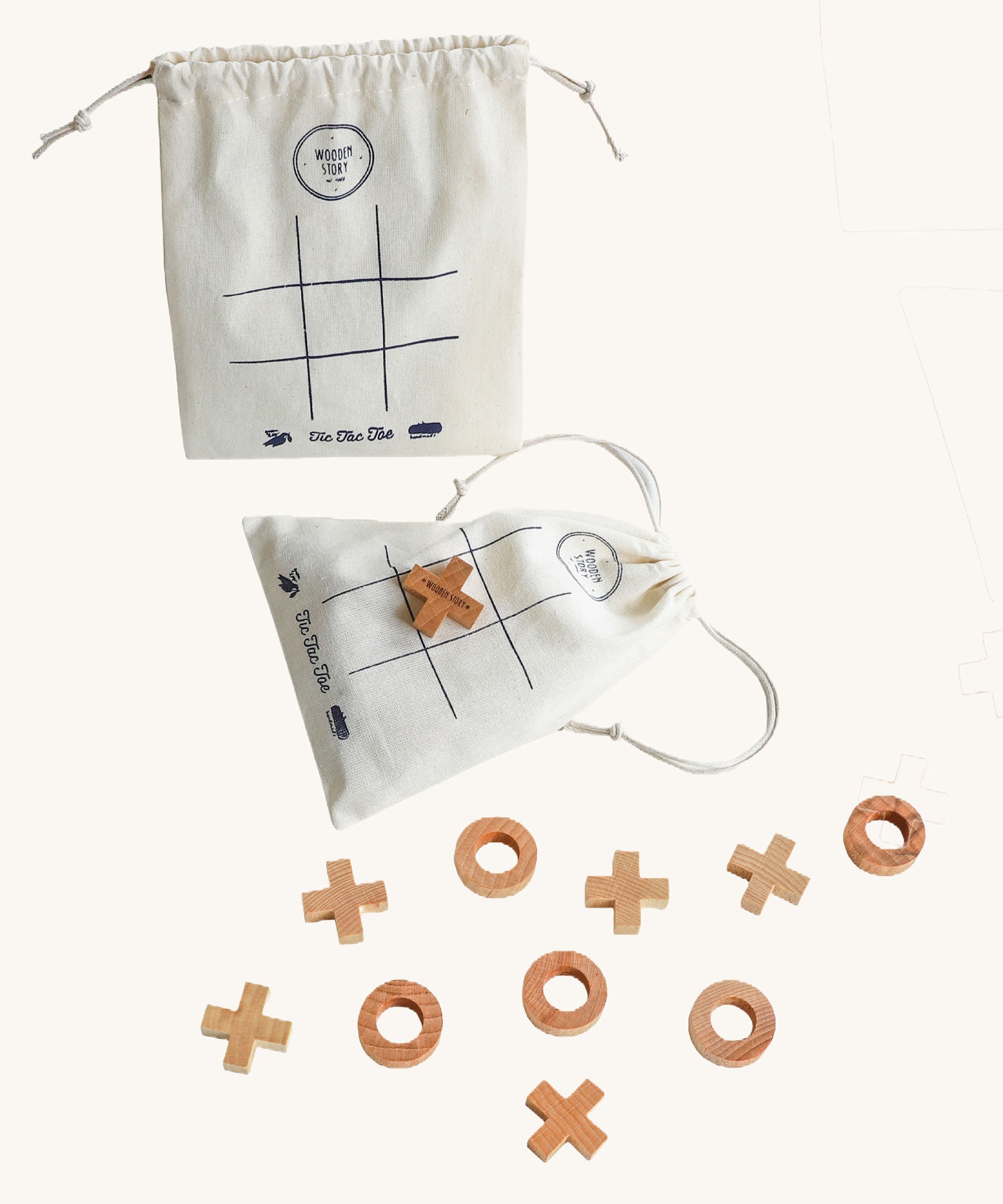 Wooden Story Tic Tac Toe game on a plain background. The wooden X and O pieces are spread out besides the drawstring bag which has the grid printed on it. One wooden X cross piece has been placed on the grid in the centre of the bag. 