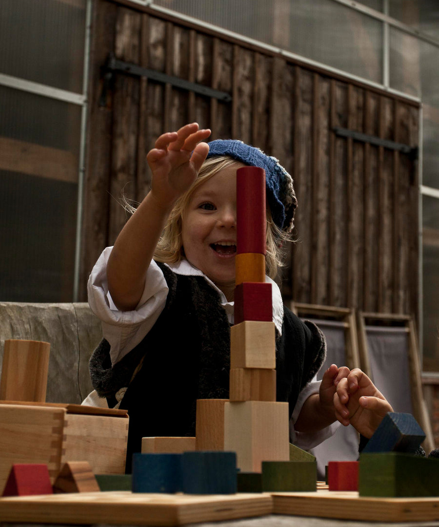 A child playing with Wooden Story Rainbow Blocks. The child is stacking the blocks on top of each other in a tower. 