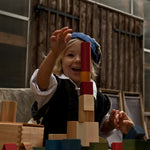 A child playing with Wooden Story Rainbow Blocks. The child is stacking the blocks on top of each other in a tower. 