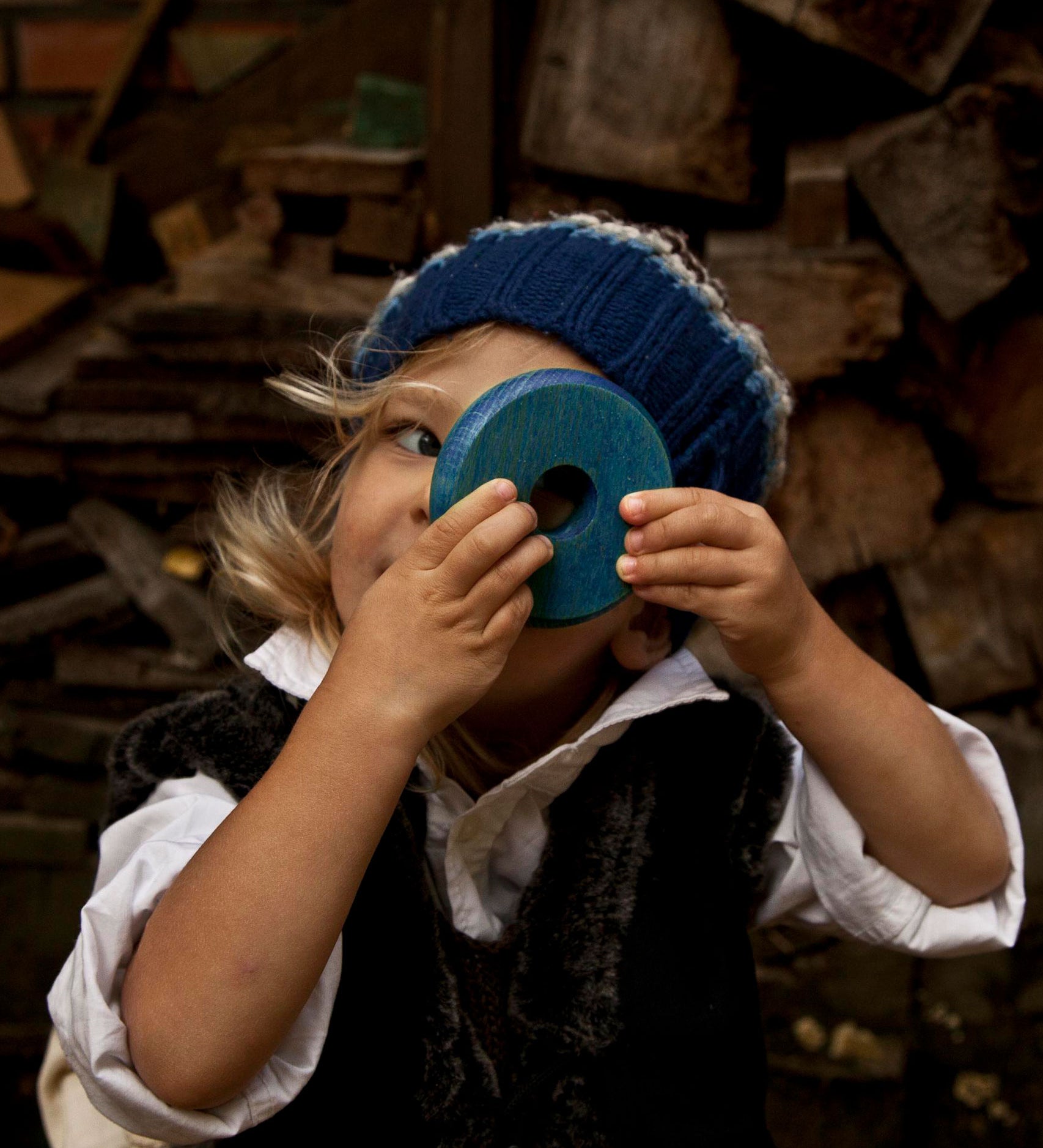 A child holding up a blue piece from the Wooden Story Rainbow Stacker up to their eye. They are peering through the hole in it's centre. 