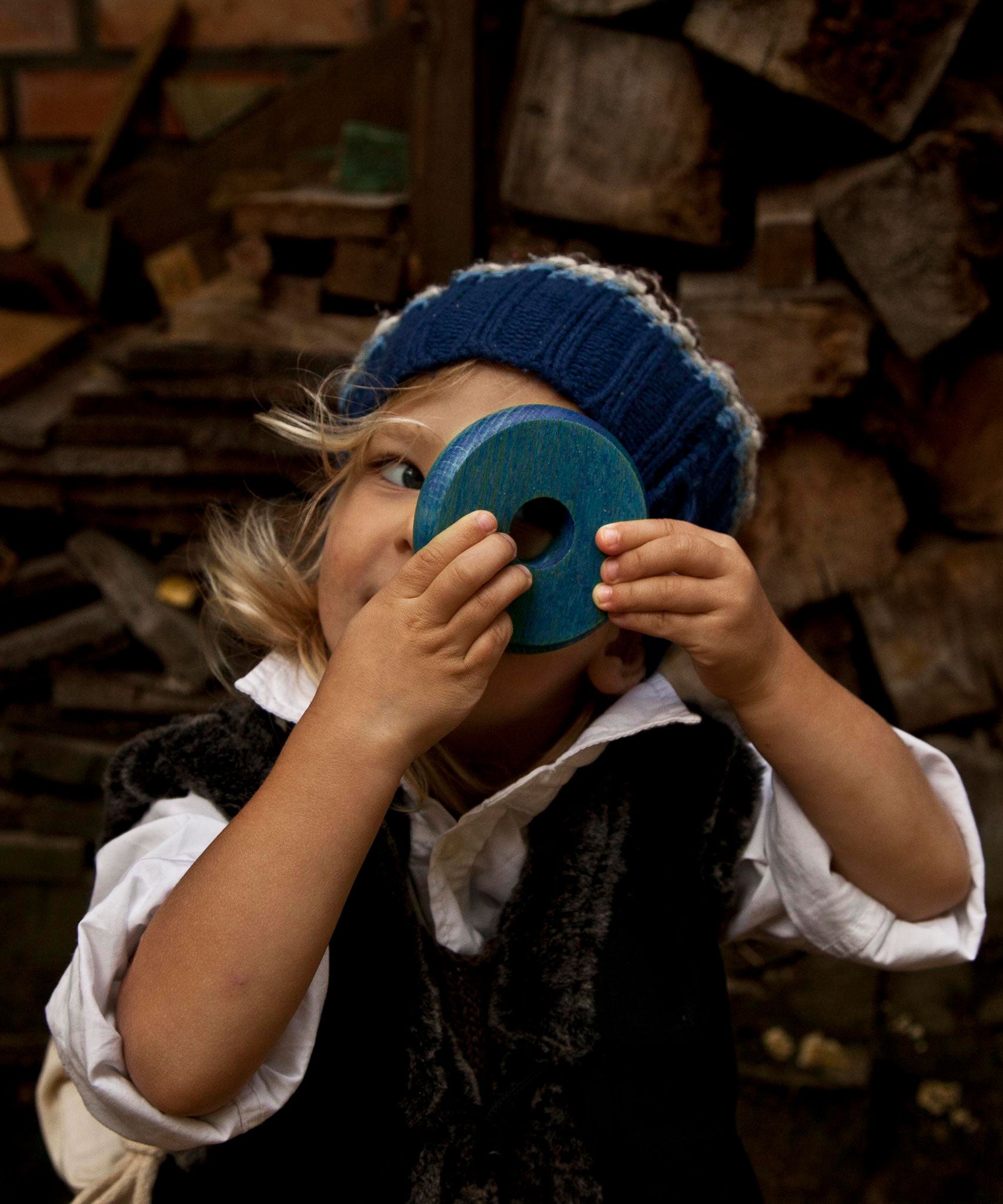 A child holding up a blue piece from the Wooden Story Rainbow Stacker up to their eye. They are peering through the hole in it's centre. 