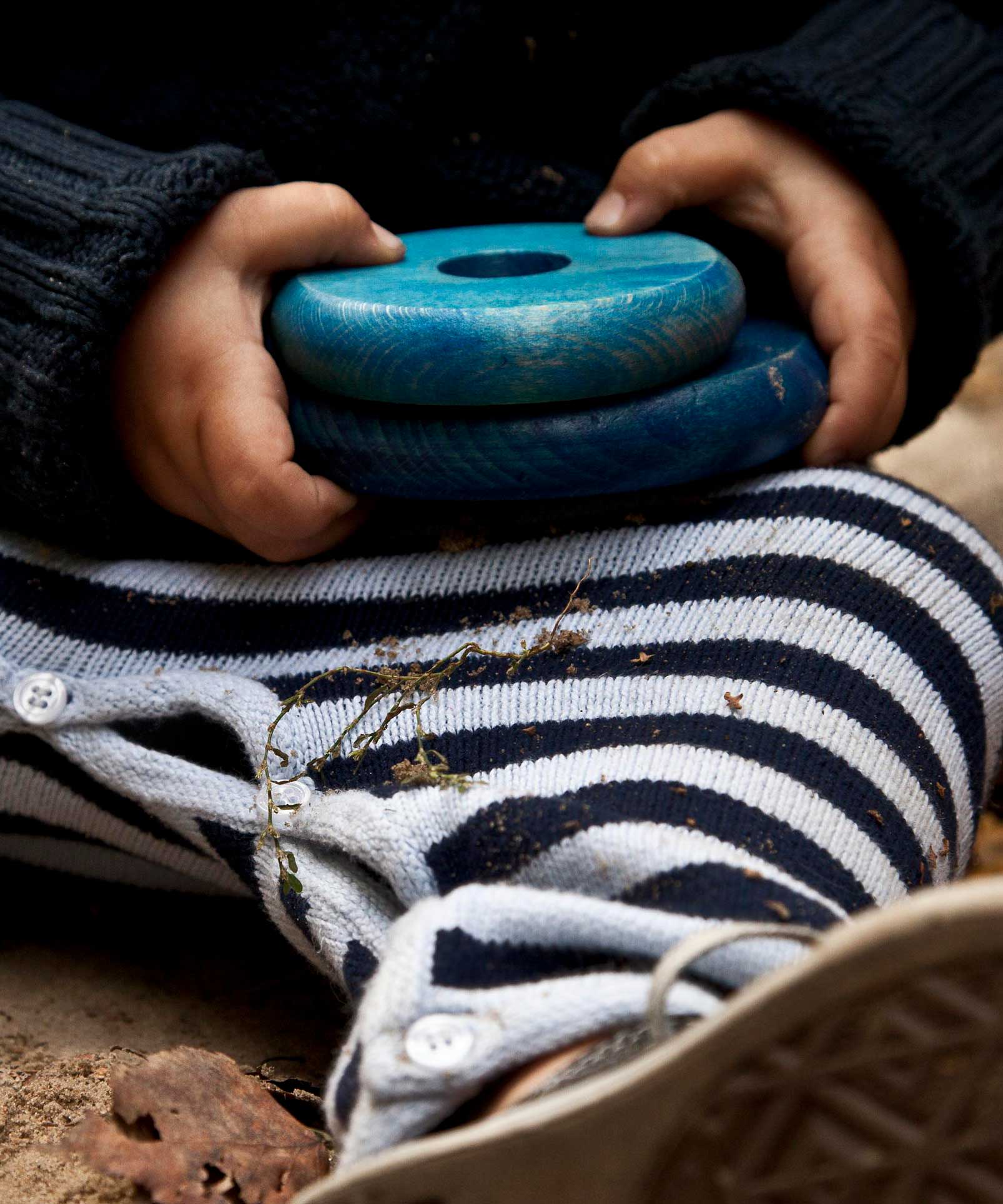 A close up of a child's hands holding to two blue pieces from the Wooden Story Rainbow Stacker.