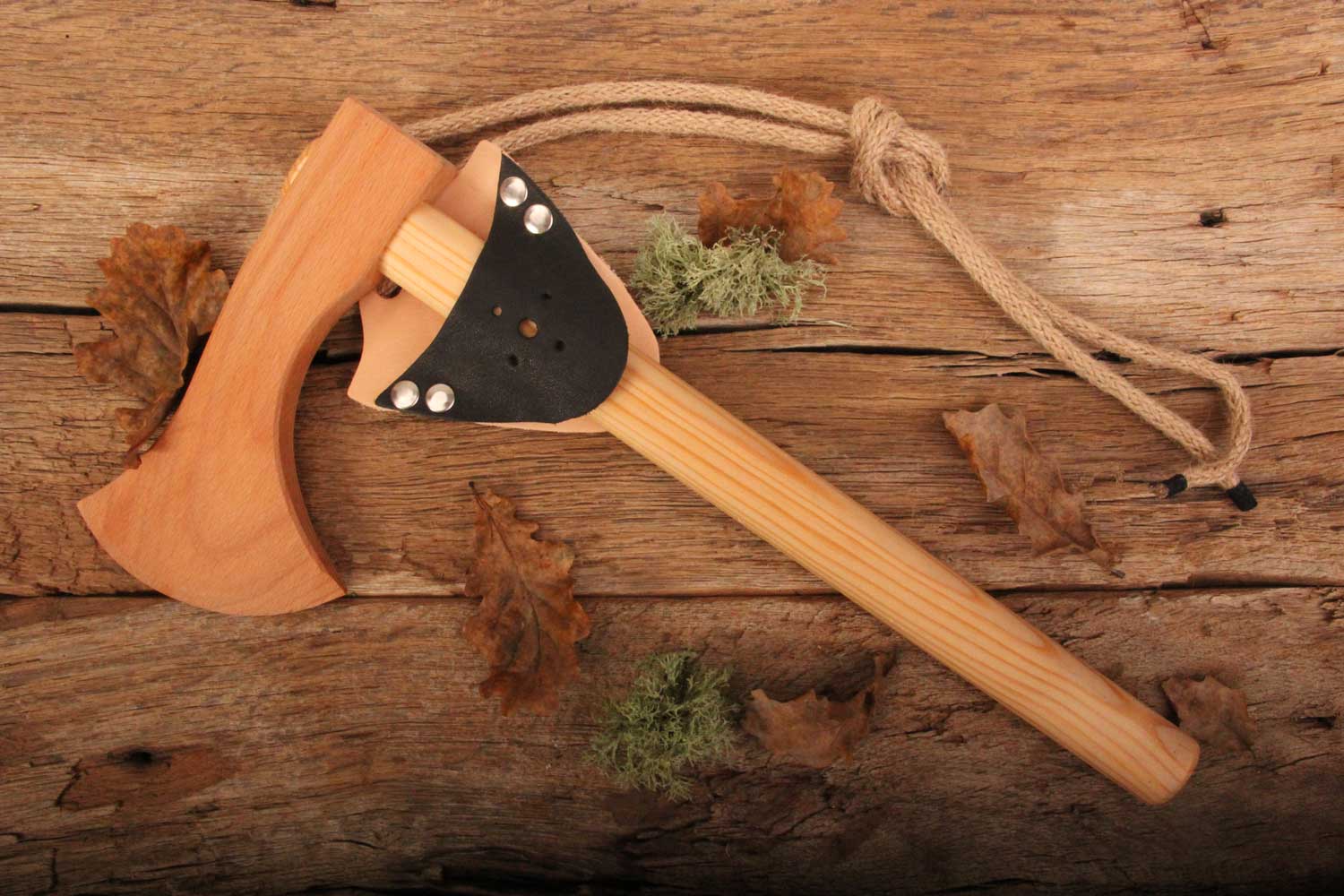 vah wooden toy battle axe pictured on a wooden surface with leaves and pieces of moss around it