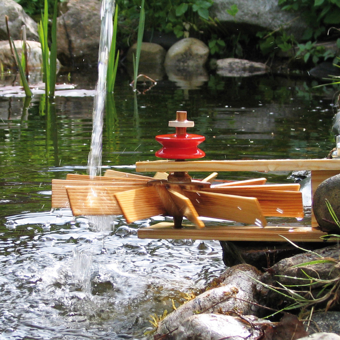 Kraul Turbine Kit being held by a rock with water flowing through the turbine wheel.