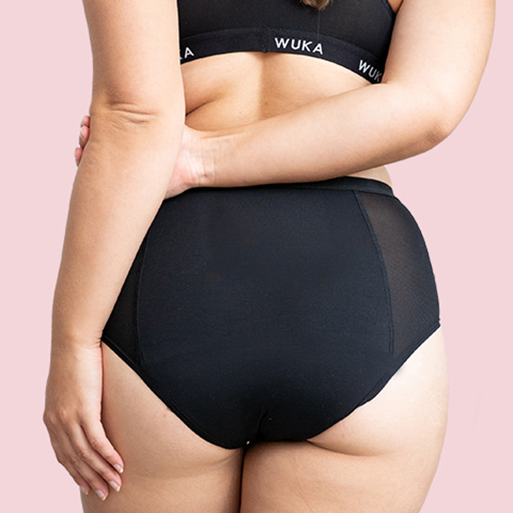 Woman stood backwards wearing the reusable WUKA high waist sanitary pants on a pink background