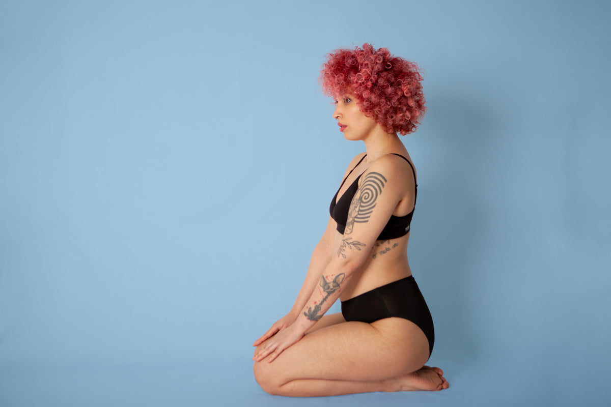 Woman on her knees wearing the eco-friendly reusable WUKA seamless midi brief sanitary pants on a blue background